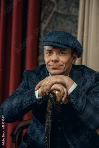 A man posing in the image of an English retro gangster of the 1920s dressed in a suit and flat cap in Peaky blinders style photo