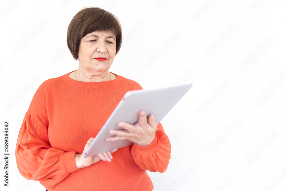 Old beautiful brunette lady looking at her tablet wearing a red sweater with white background Old beautiful brunette lady looking at her tablet wearing a red sweater with white background