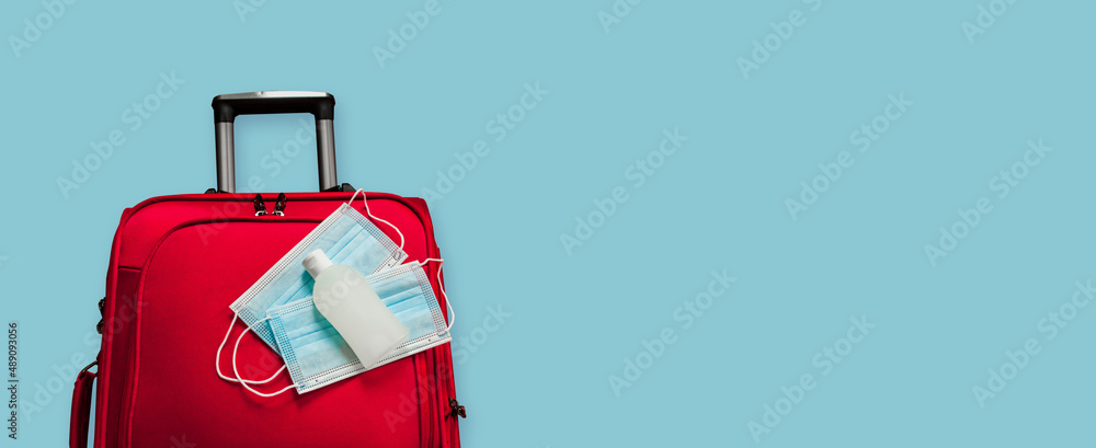 Medical face masks and antiseptic on a red suitcase, safe travel after the pandemic. Coronavirus free worldwide traveling, new normal lifestyle concept. flat lay, top view, banner, blue background