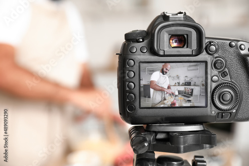 Handsome man making dough on display of photo camera in kitchen  closeup