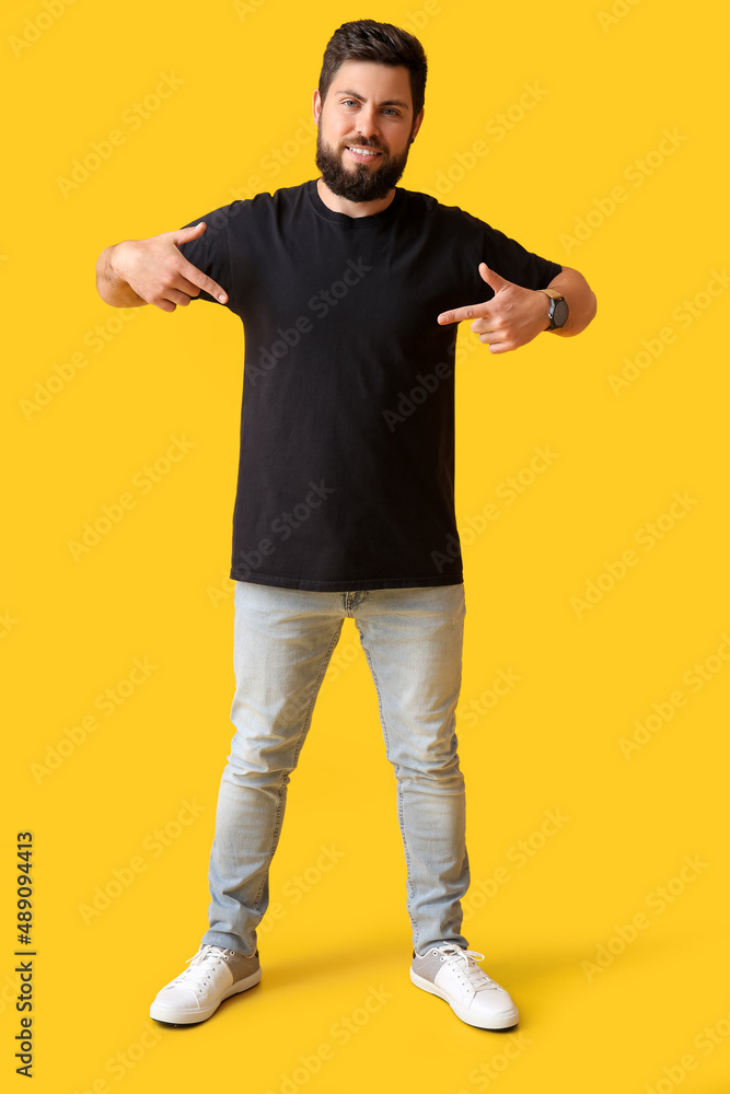 Handsome man pointing at black t-shirt on yellow background Handsome man pointing at black t-shirt on yellow background