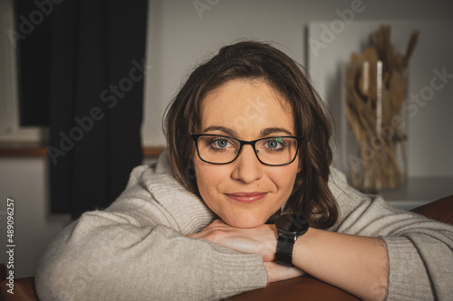 Portrait of a young, pretty, emotional surprised business woman, looking through glasses, sitting on a chair, in a bright room