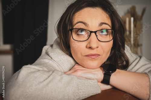 Portrait of a young, pretty, emotional surprised business woman looking aside with glasses sitting on a chair in a bright room 