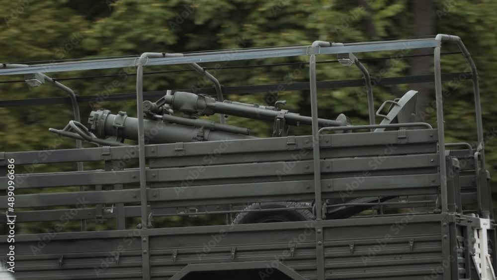 Mortar on wheels is transported in the back of military truck, close-up. Army vehicle drives along green street of city. Redeployment of military weapons and troops. Mortar on wheels is transported in the back of military truck, close-up. Army vehicle drives along green street of city. Redeployment of military weapons and troops.