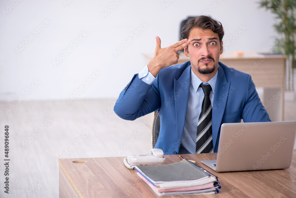 Young male employee unhappy with excessive work in the office Young male employee unhappy with excessive work in the office