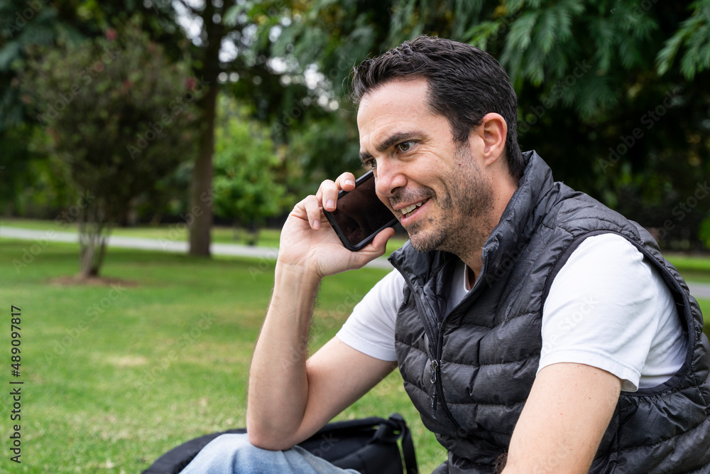 White Hispanic man using phone at park. Middle aged man talking by phone outdoors. White Hispanic man using phone at park. Middle aged man talking by phone outdoors.