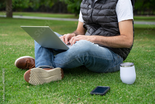 Caucasian man sitting on grass working with laptop at a park. Middle aged man working outdoors.