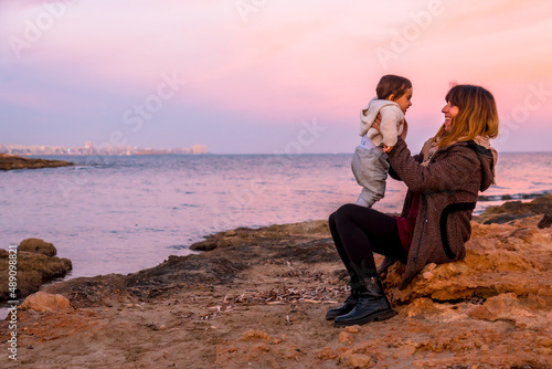 Lifestyle of a family on the beach, a baby having fun with his mother sitting by the sea at sunset