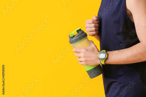 Sporty man with fitness tracker and bottle of water on color background, closeup