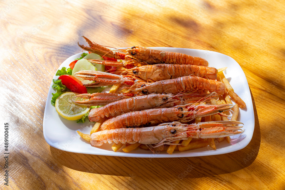 Fried langoustines with french fries and lemon on the table at sunny day Fried langoustines with french fries and lemon on the table at sunny day