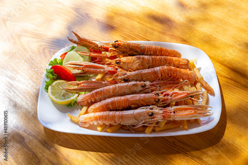 Fried langoustines with french fries and lemon on the table at sunny day