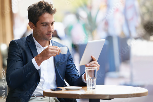 Catching up online with an expresso. Shot of a young businessman sitting at an outdoor cafe using a digital tablet. photo