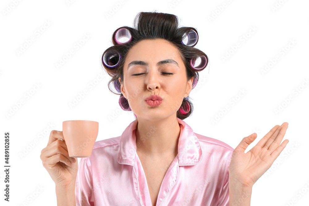 Beautiful young woman in pajamas and hair curlers drinking coffee on white background Beautiful young woman in pajamas and hair curlers drinking coffee on white background