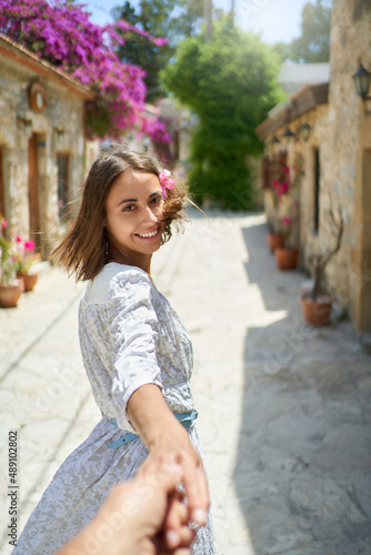 Smiling beautiful woman with flower in hair wearing white dress holding hand of her boyfriend, enjoying walking during vacation © vitaliymateha