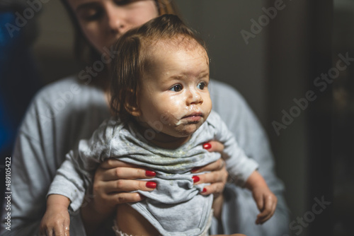 unknown mother holding her baby nasty small caucasian child little girl with food around her mouth and on dirty face making mess at home childhood and growing up concept copy space growing up photo