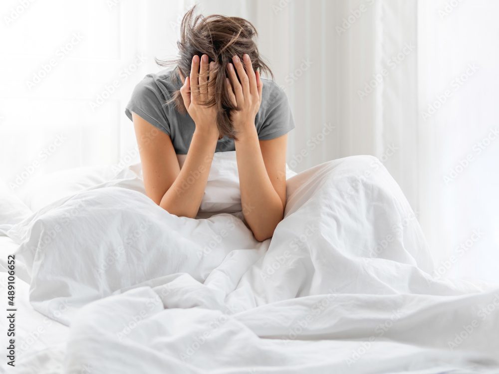 Sleepy woman with hands in hair is sitting in bed . Woman in depression or suffer of headache. Sleepy woman with hands in hair is sitting in bed . Woman in depression or suffer of headache.