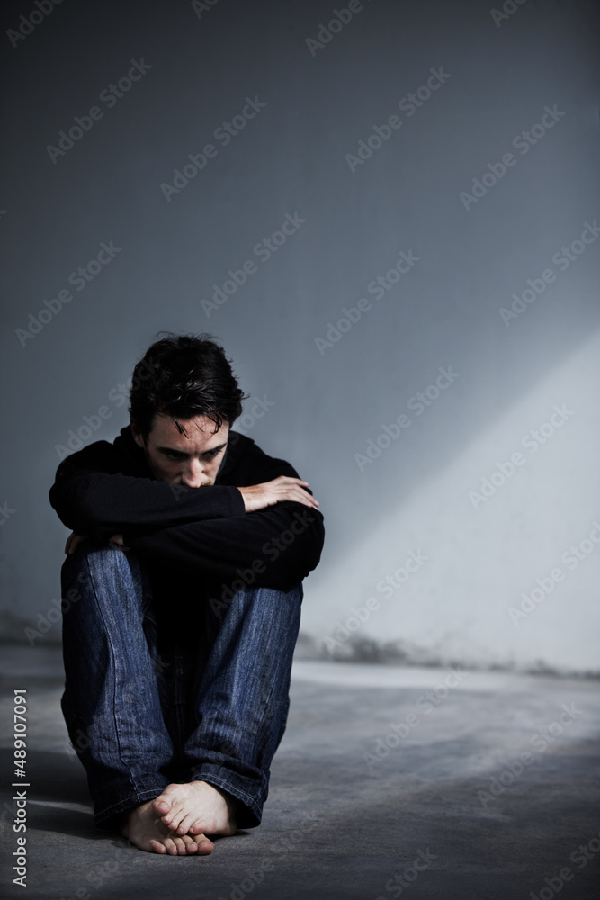 Dealing with emotional stress. A young man looking worried while sitting barefoot on the ground.