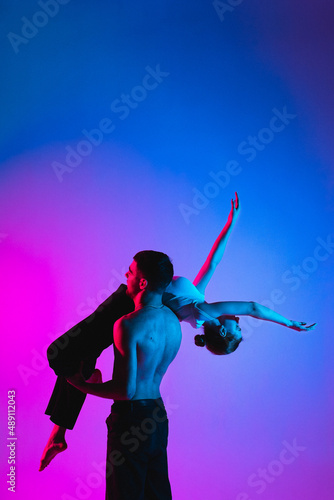 Gymnastics support. A man with a girl perform an acrobatic exercise, neon light