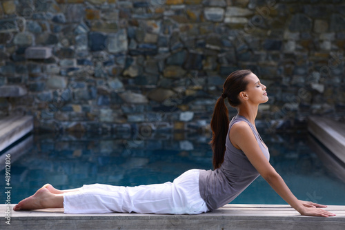 Perfecting the upward facing dog position. A beautiful young woman doing yoga beside a pool.