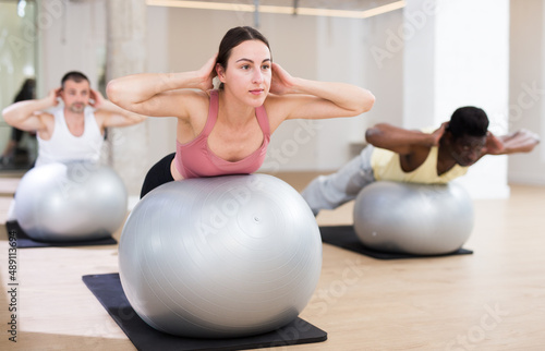 Young sporty woman doing exercises with pilates ball during group training at gym