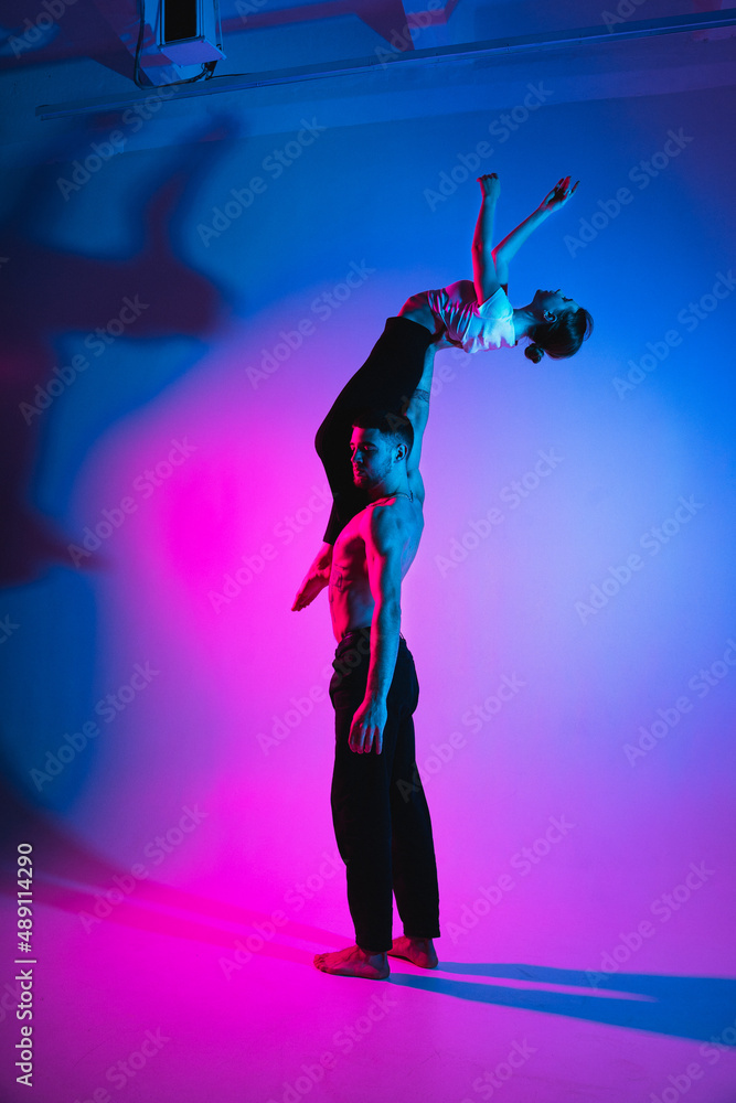 Gymnastics support. A man with a girl perform an acrobatic exercise, neon light