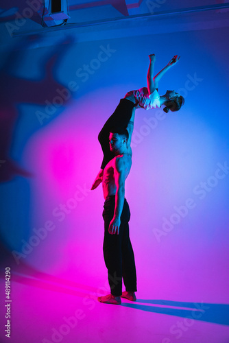 Gymnastics support. A man with a girl perform an acrobatic exercise, neon light