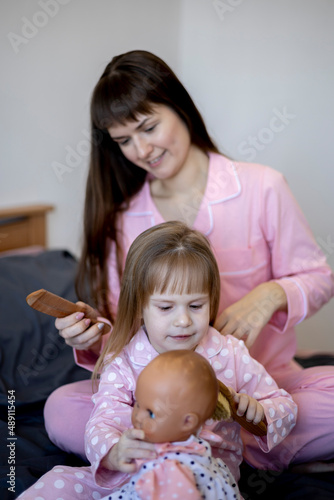 Mother combs her little daughter's hair while sitting in bed in morning. Good morning.