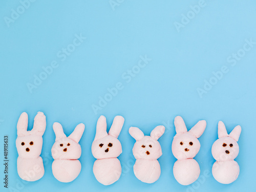 Pink handmade marshmallow candy bunnies on blue paper background with copy space for your Easter text message. Minimal happy Easter holiday conceprt. Top view flat lay, border frame.