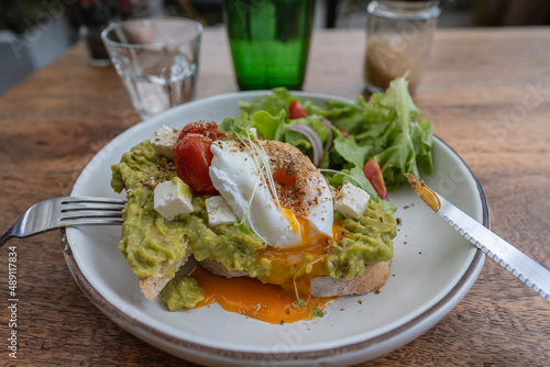 Sourdough toast, poached eggs, avocado pulp and fresh vegetables on plate in cafe, close up