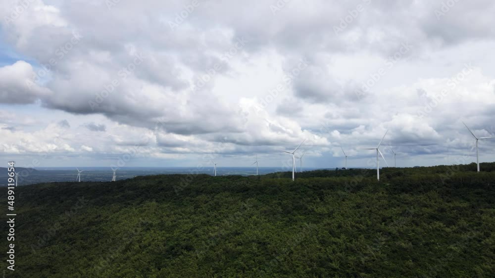 Top view on the green mountain there is windmill spinning. The sky was filled with thick gray clouds.