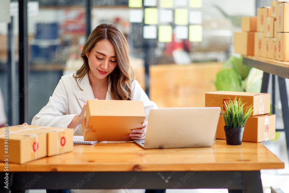 Startup SME small business entrepreneur SME or freelance Asian woman using a laptop with box, Young success Asian woman with her hand lift up, online marketing packaging box and delivery, SME concept. Startup SME small business entrepreneur SME or freelance Asian woman using a laptop with box, Young success Asian woman with her hand lift up, online marketing packaging box and delivery, SME concept.