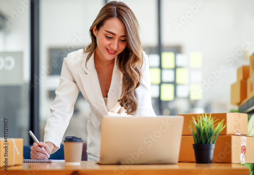 Startup SME small business entrepreneur SME or freelance Asian woman using a laptop with box, Young success Asian woman with her hand lift up, online marketing packaging box and delivery, SME concept. © David