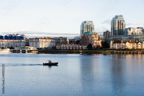 Small boat from the harbour patrol cruising along during a sunny early morning with buildings in the background, Victoria, British Columbia, Canada © Anne Richard