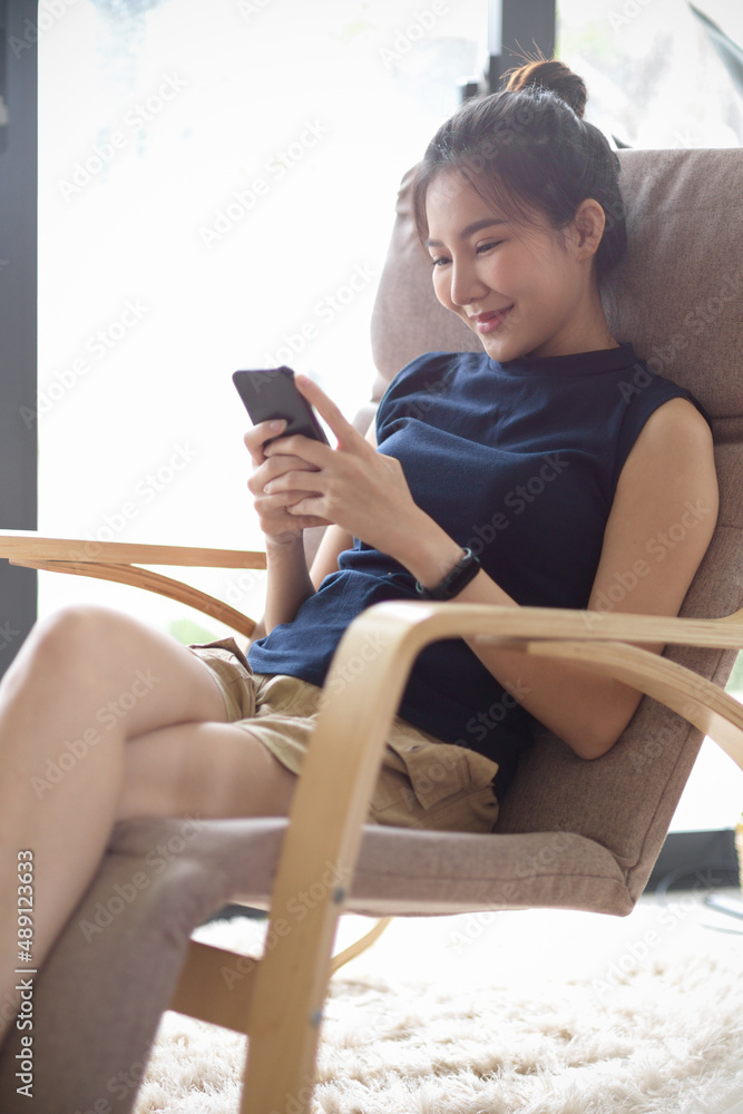 Obraz premium Woman sits in modern and comfy armchair, using smartphone