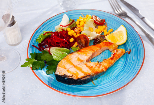 Grilled salmon steak with vegetable salad, made from corn, cherry tomatoes, lettuce leaves and grated beetroot, served with ..a slice of lemon