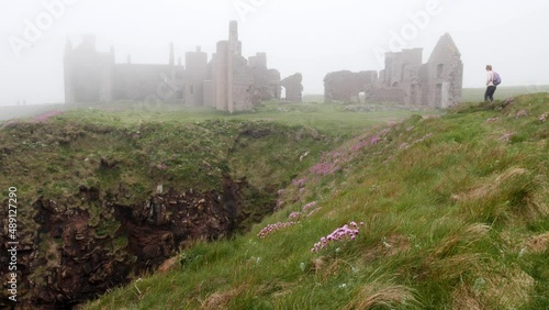 Lady walker approaches Slains Castle from the north past a steep gully photo