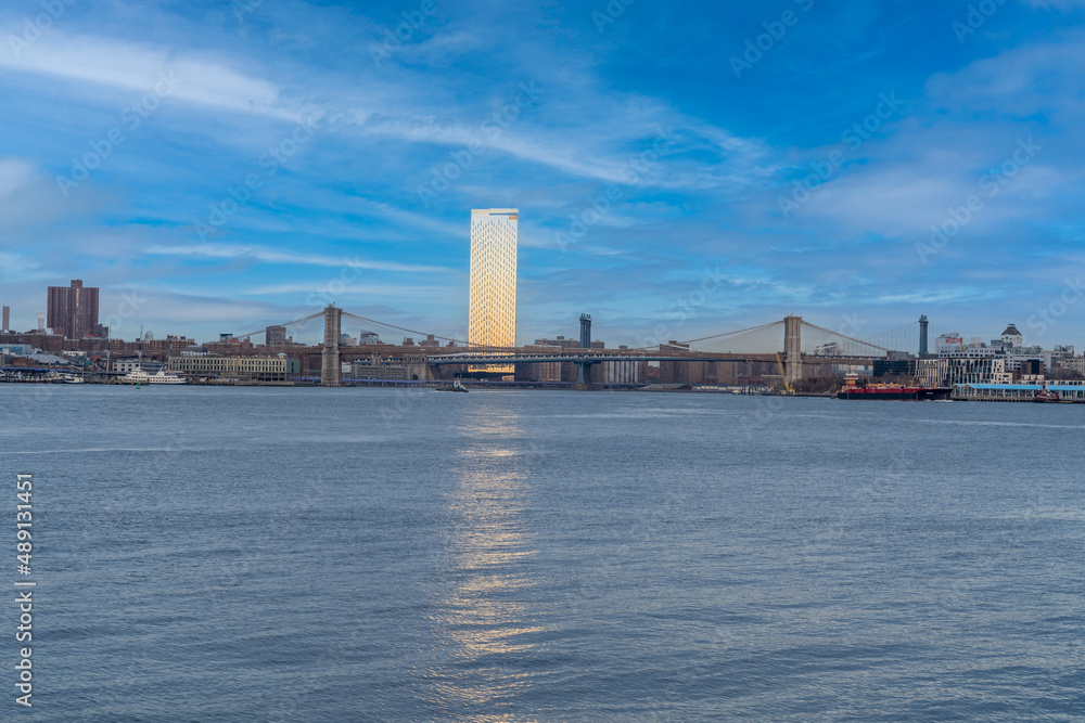 View of the Brooklyn bridge in New York from across Governors Island with shiny skyscraper reflecting the sun