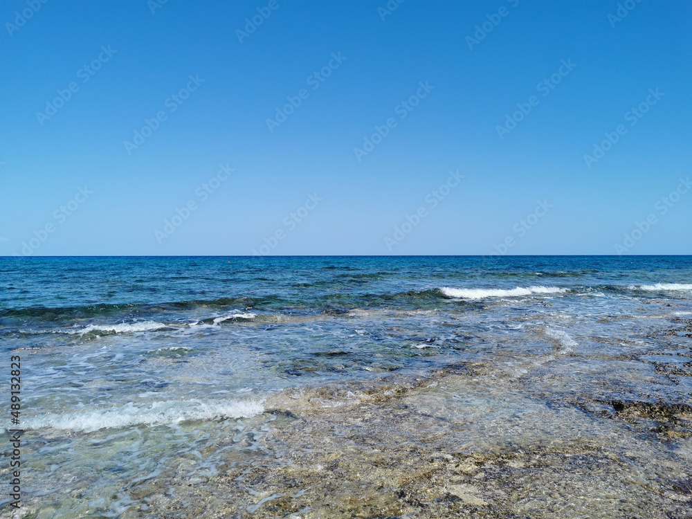 The coast of the Mediterranean Sea, waves, clear water, through which you can see the stone bottom. All this against a blue sky with clouds. The coast of the Mediterranean Sea, waves, clear water, through which you can see the stone bottom. All this against a blue sky with clouds.