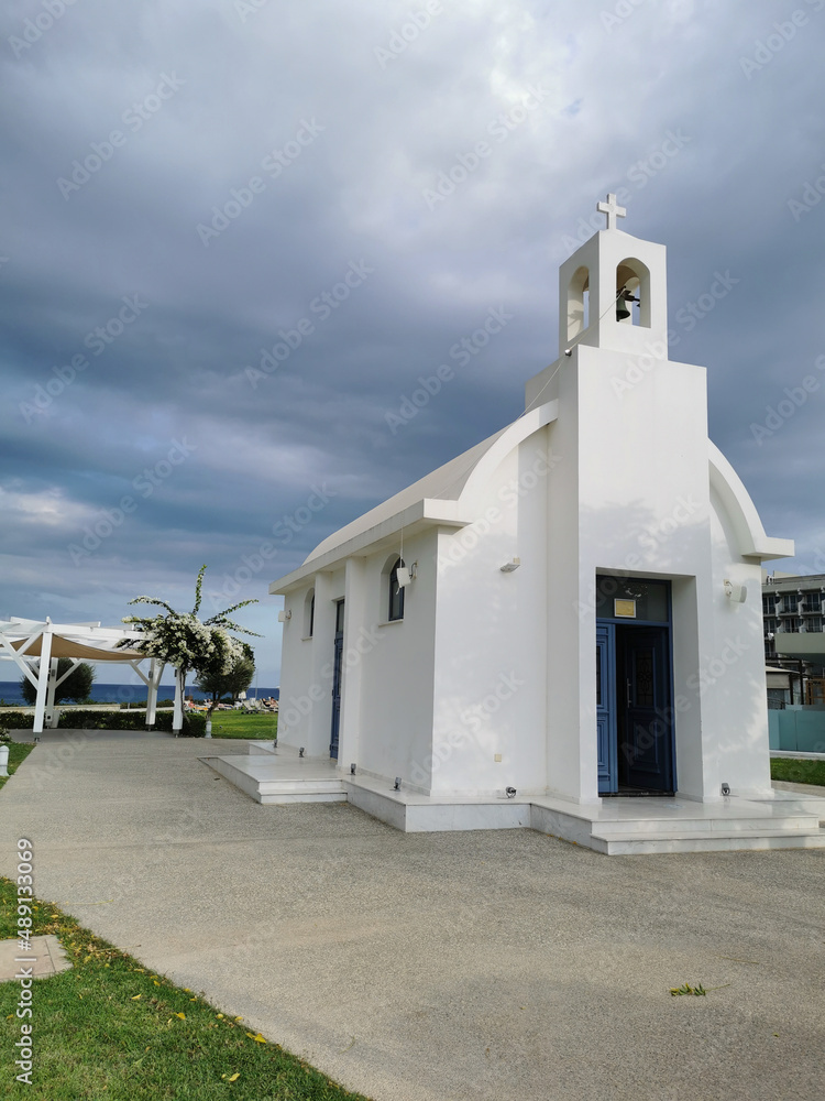 The open white Chapel of St. Constantine and St. Helena on the seafront against a dramatic sky..flowering shrub on the streets of Protaras against a blue sky with clouds.