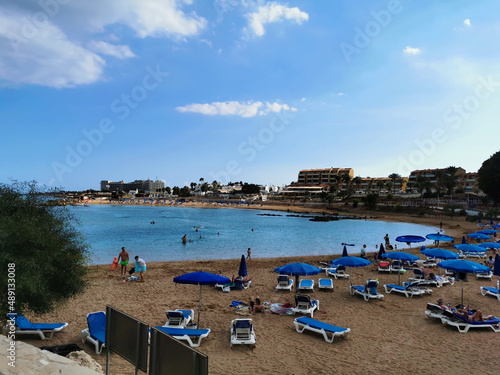 Protaras. Famagusta area. Cyprus. Sandy Kalamies beach with sun loungers and parasols in the bay of the Mediterranean Sea in the background of a blue sky with clouds. © Elena