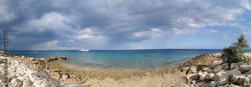 Panorama. The stone coast of the Mediterranean Sea, a white pleasure ship in the sea against a dramatic sky. with clouds.