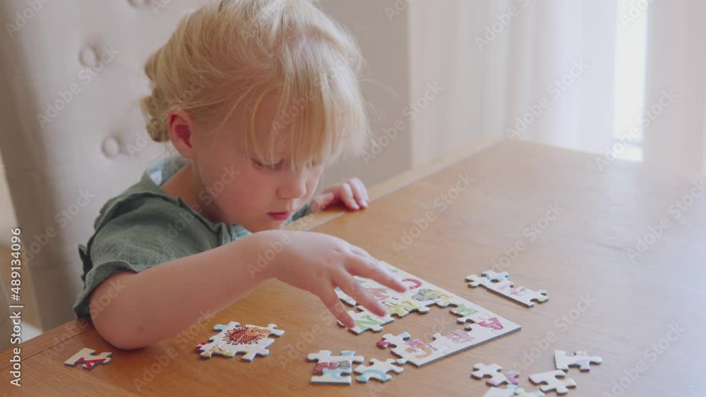 Young girl having fun sitting at table at home doing jigsaw puzzle - shot in slow motion Young girl having fun sitting at table at home doing jigsaw puzzle - shot in slow motion