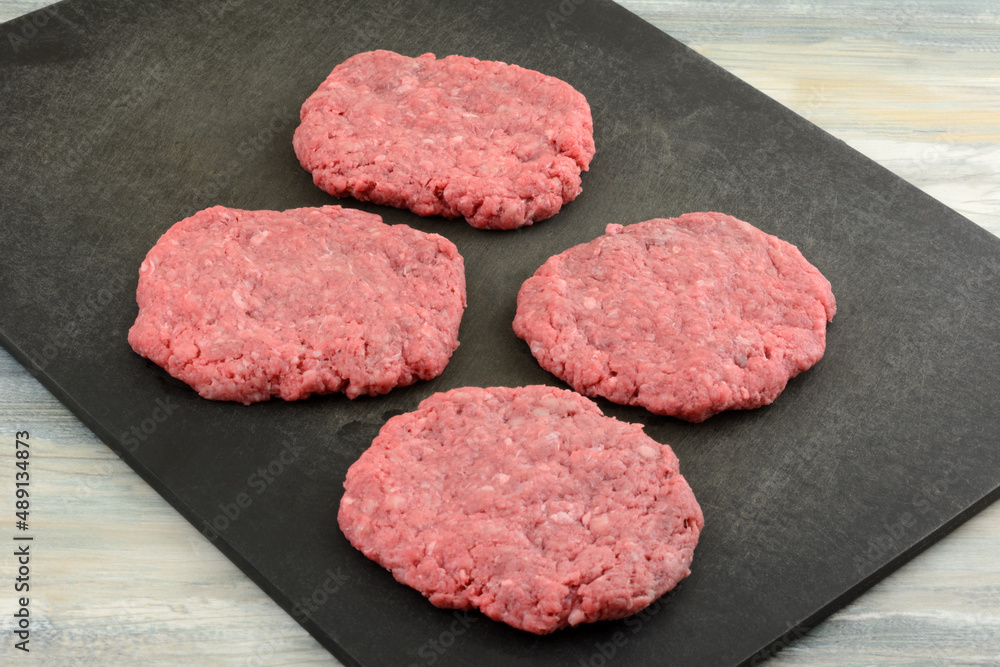 Raw formed ground beef hamburger patties on black cutting board Raw formed ground beef hamburger patties on black cutting board