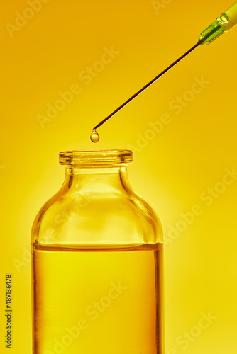 A drop of liquid drips from the needle of a medical syringe into the bottle. Front view. Macro photo.