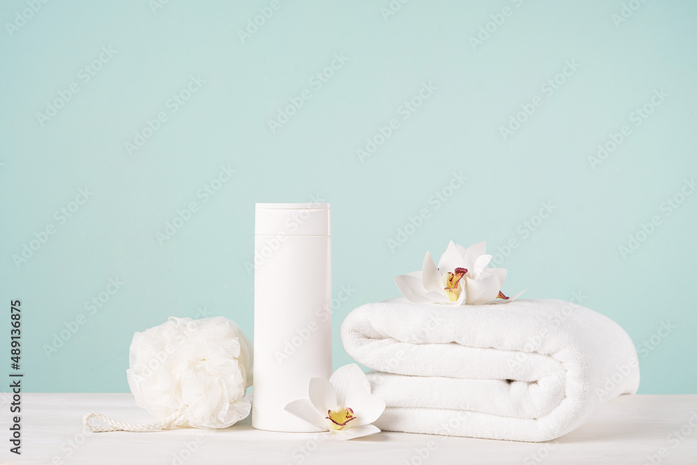 A folded white towel, a bottle of shampoo or shower gel, a washcloth and orchid flowers on a light blue background. Bath mockup with copy space. A folded white towel, a bottle of shampoo or shower gel, a washcloth and orchid flowers on a light blue background. Bath mockup with copy space.