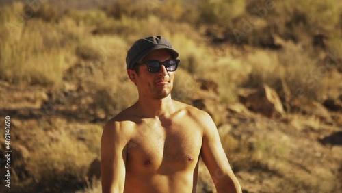 Close up front view of a young shirtless American boy in sunglasses firing two handguns rapidly. photo