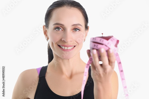 Happy sportswoman holds an apple wrapped with measuring tape
