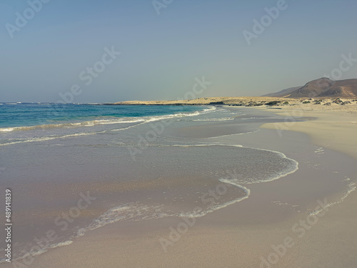 Atlantic Ocean view from a hill in Cape Verde. Rough desert terrain with hiking trails, blue afternoon sky. Selective focus on the details, blurred background.