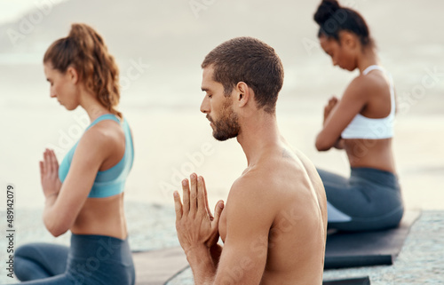 Take the moment to be present and at peace. Shot of a group of young people practicing yoga together outdoors.