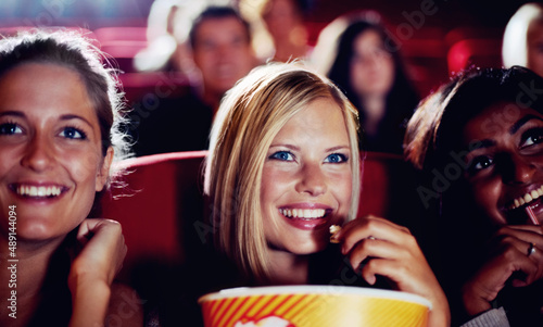 Girls night. Three friends laughing during a movie while eating popcorn.